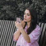 A woman in a pink shirt applying lip gloss using a small patterned mirror